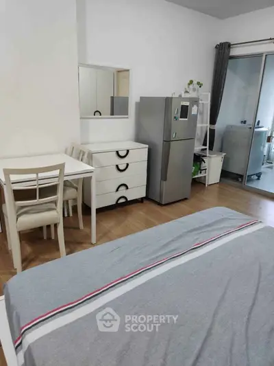 Cozy studio apartment with modern furniture and appliances, featuring a compact dining area and sleek refrigerator.