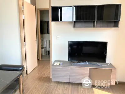 Modern living room with sleek TV unit and wooden flooring, leading to a cozy hallway and a well-equipped bathroom.