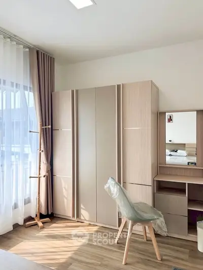 Bright bedroom with modern wardrobe and vanity set, featuring natural light and elegant curtains.