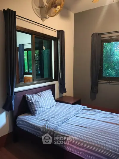 Cozy bedroom with single bed and large windows offering lush green views.