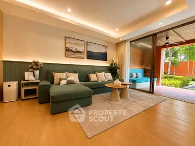 Spacious living room with modern decor and garden view, featuring a cozy green sofa and elegant wooden flooring.