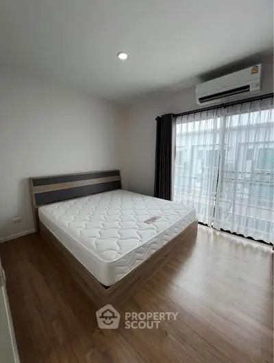 Modern bedroom with large window and air conditioning, featuring a minimalist design and wooden flooring.