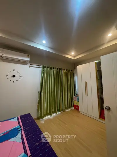 Cozy bedroom with modern decor, featuring wooden flooring and ample natural light through large windows.