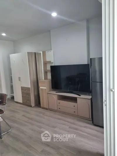 Modern living room with sleek furniture and large TV, featuring a stylish wardrobe and stainless steel fridge.