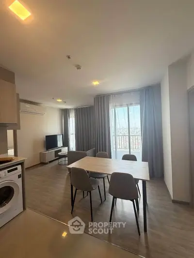 Modern living room with dining area and washing machine, featuring large windows and stylish decor.