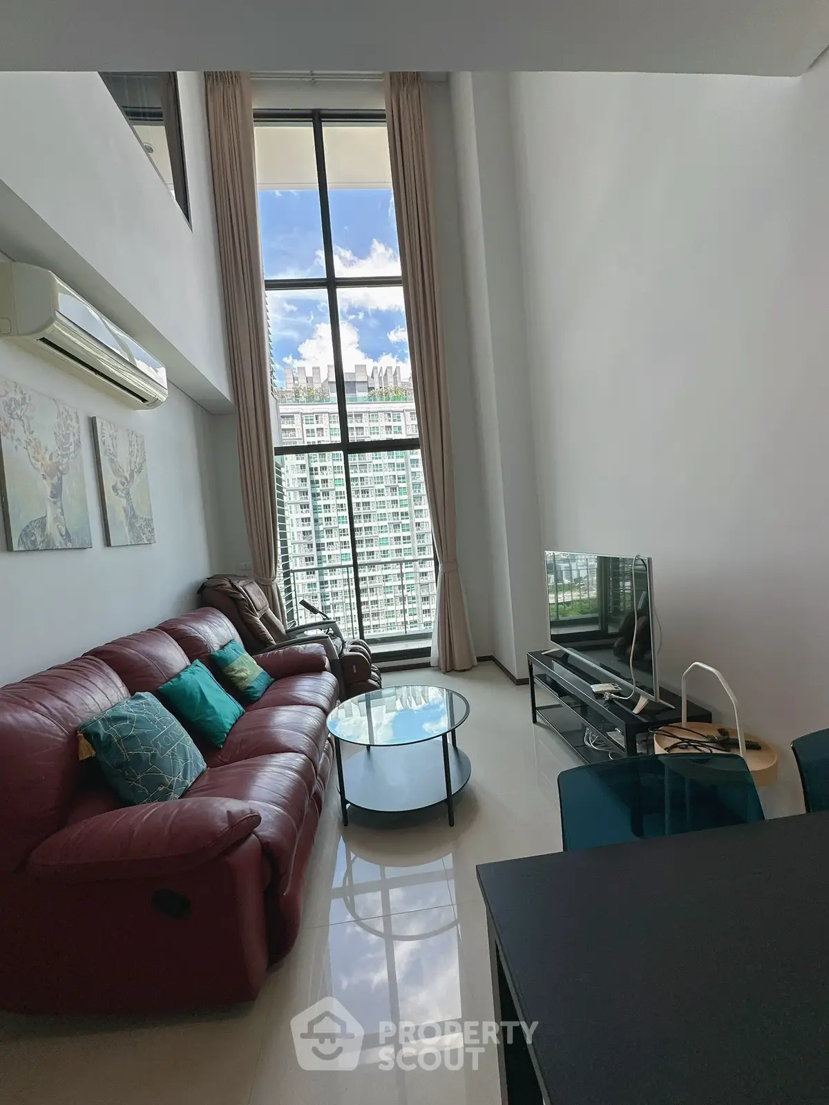 Spacious living room with high ceiling and large window offering stunning city views, featuring modern furniture and decor.