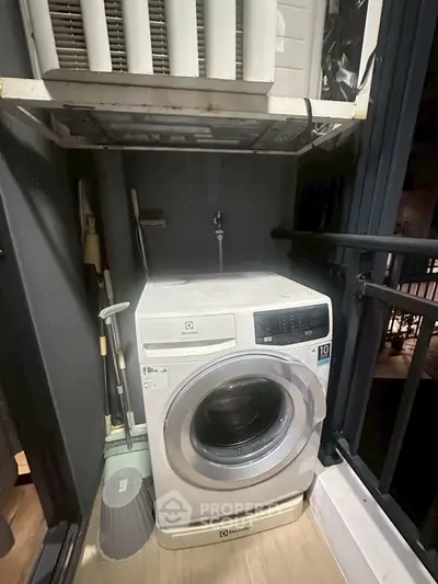 Compact laundry area with washing machine and cleaning tools on a balcony.