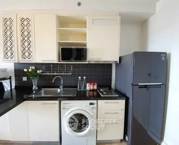 Modern kitchen with washing machine, fridge, and microwave in compact layout.