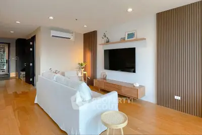 Modern living room with wooden flooring, stylish furniture, and wall-mounted TV in a cozy apartment.