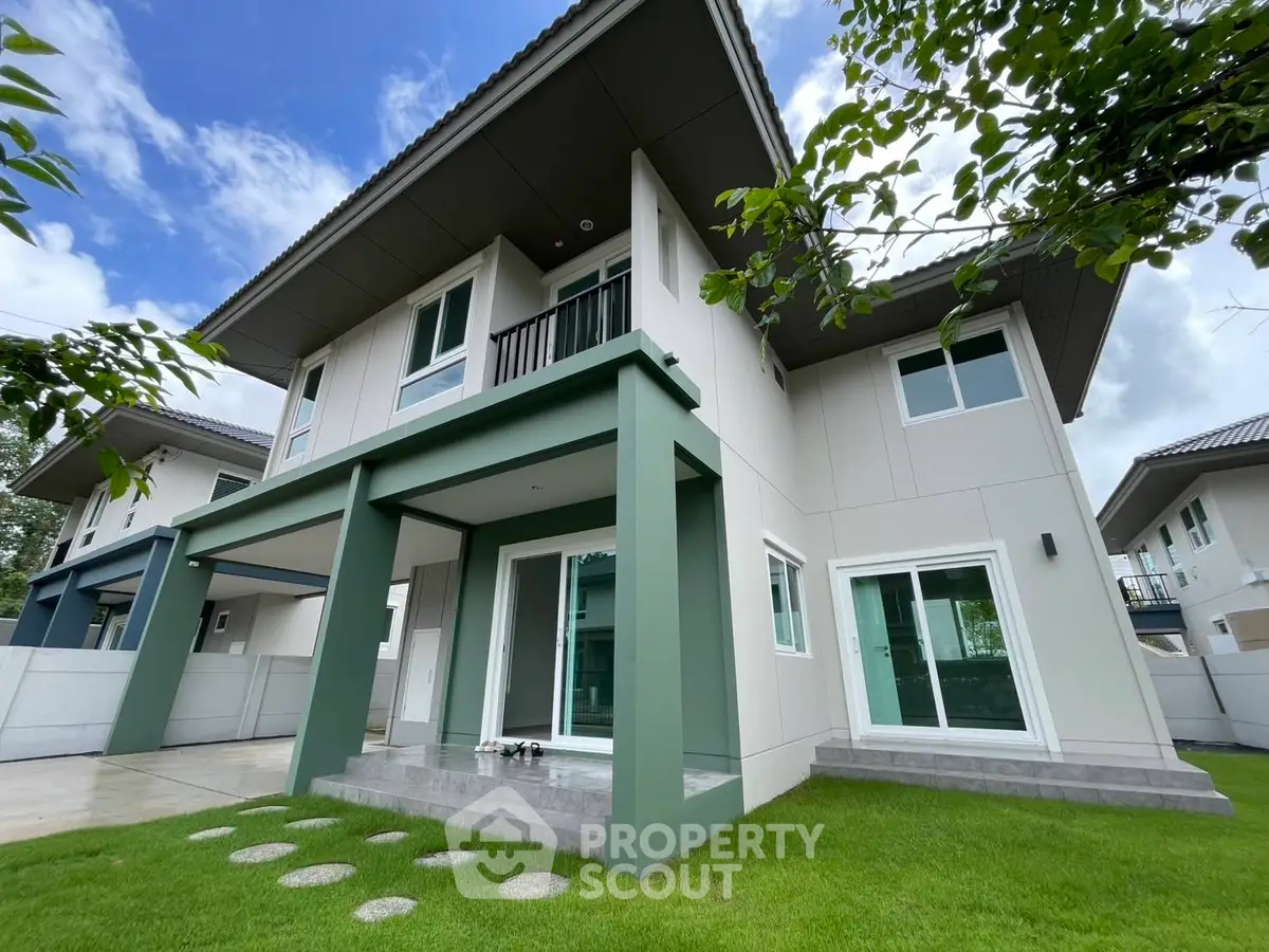 Modern two-story house with green accents and lush lawn under a clear blue sky.