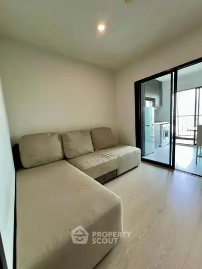 Modern living room with beige sofa and glass sliding doors leading to kitchen.