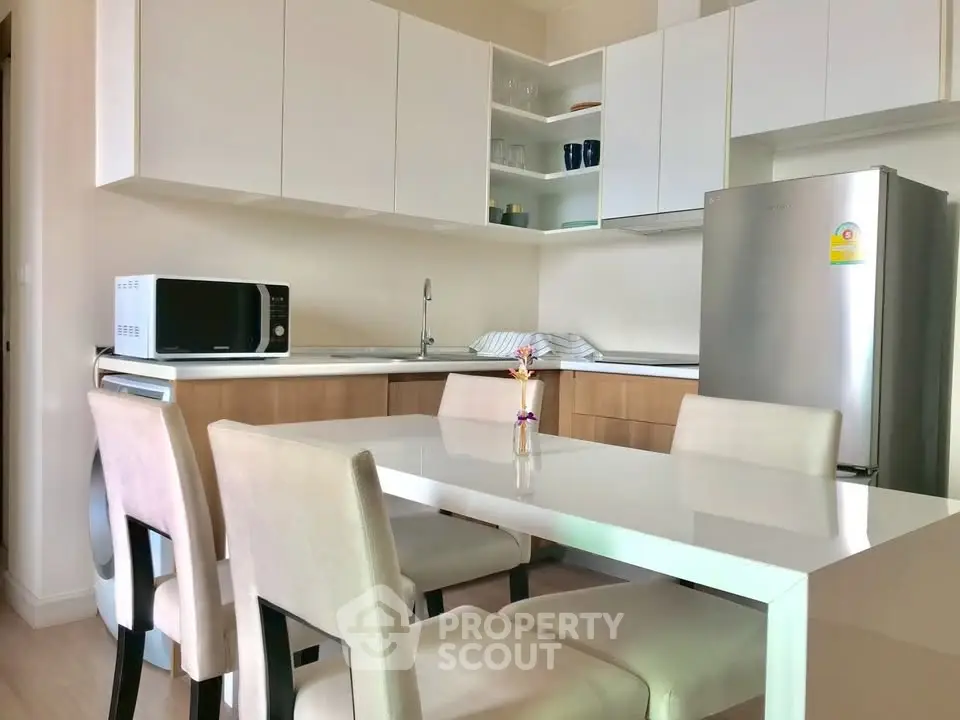 Modern kitchen with sleek cabinetry, dining table, and stainless steel fridge in a cozy apartment.