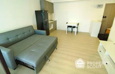 Modern living room with sleek sofa and compact kitchen area in open layout apartment.