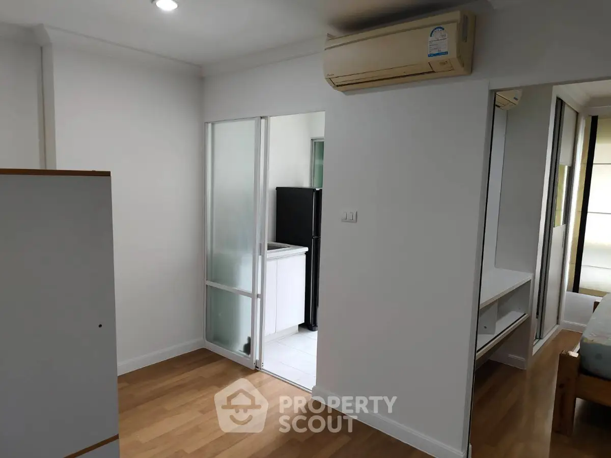 Modern apartment interior with wooden flooring and air conditioning, featuring a compact kitchen area.