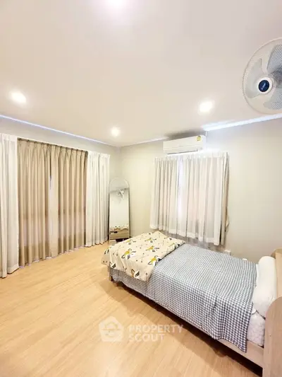 Spacious bedroom with cozy single bed, large windows, and elegant curtains.