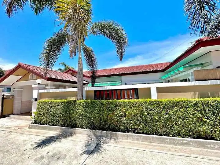 Charming tropical villa with lush greenery and red-tiled roof under clear blue sky.
