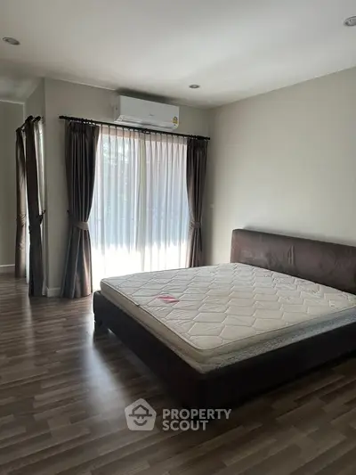 Spacious bedroom with large windows and natural light, featuring a comfortable bed and elegant curtains.