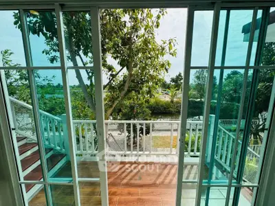 Charming balcony view with lush greenery and glass doors, perfect for relaxation and enjoying nature.