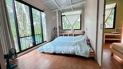 Spacious bedroom with large windows and serene forest view, featuring minimalist decor and wooden flooring.