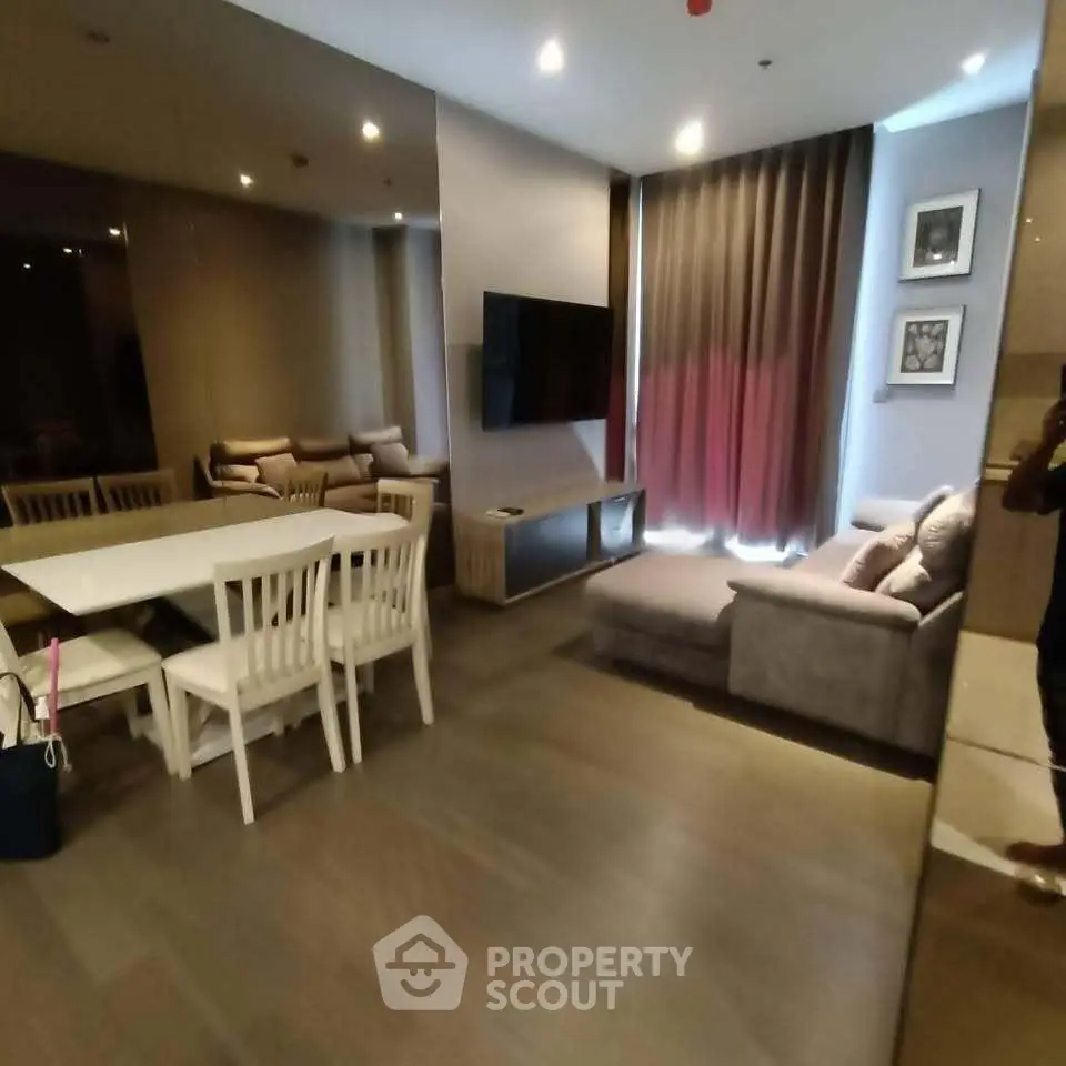 Modern living room with sleek furniture and dining area, featuring a wall-mounted TV and elegant decor.