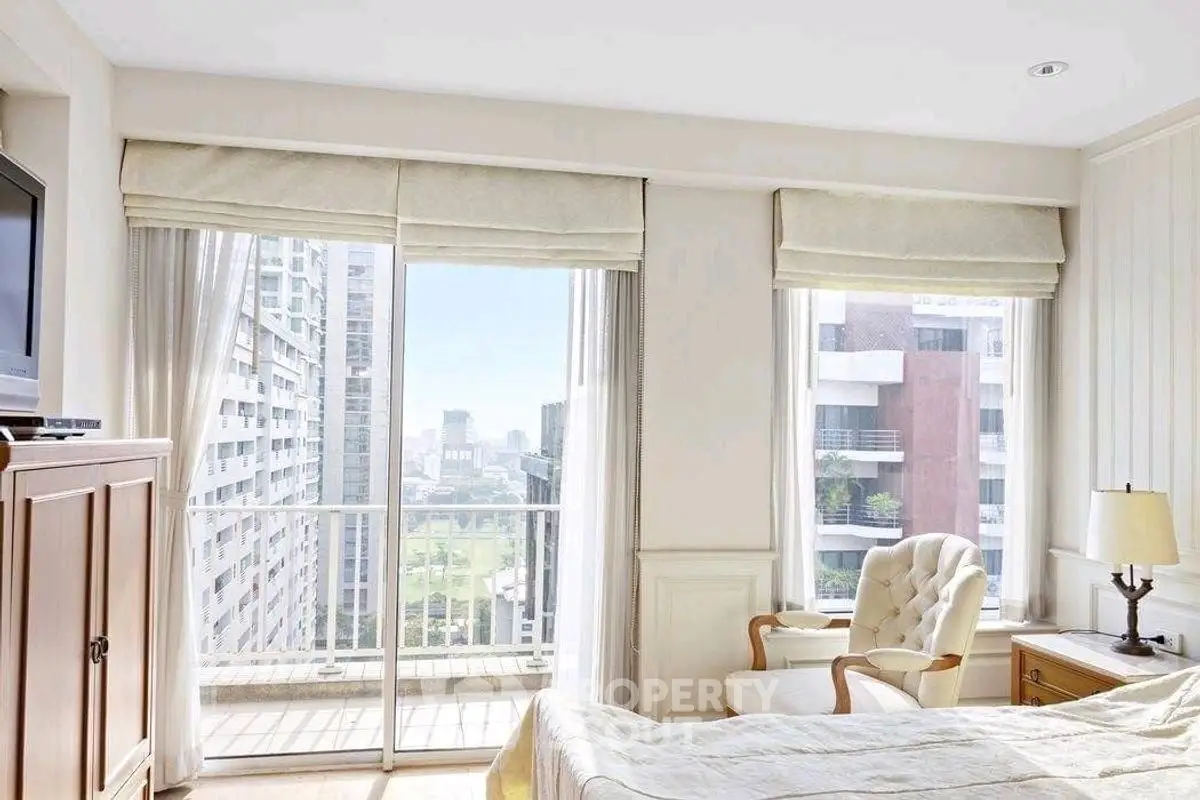 Bright bedroom with balcony and city view, featuring cozy armchair and elegant decor.