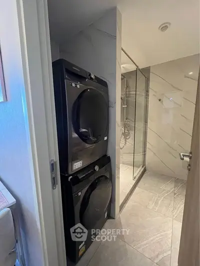 Modern bathroom with stacked washer and dryer next to a glass-enclosed shower.