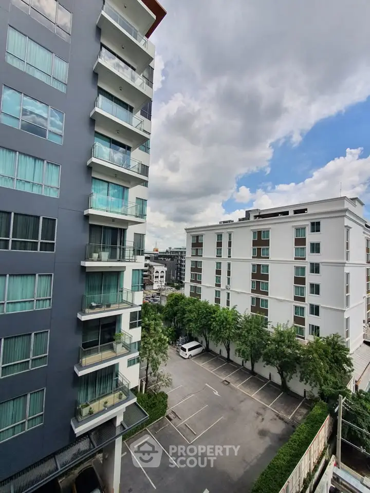 Modern apartment buildings with spacious parking and lush greenery under a vibrant sky.