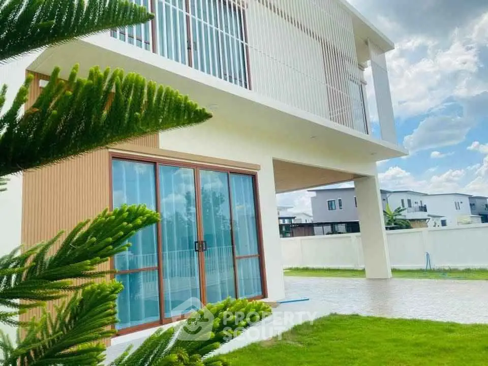 Modern two-story house with large windows and lush green lawn under a clear blue sky.