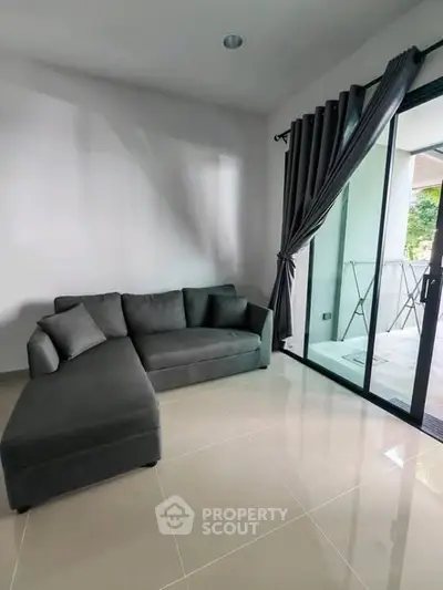 Modern living room with sleek gray sofa and large glass doors opening to a balcony.
