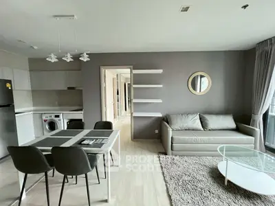 Modern living room with dining area and kitchen, featuring sleek furniture and neutral tones.