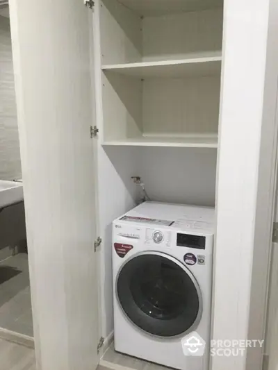 Modern laundry area with built-in washing machine and storage shelves in sleek apartment.