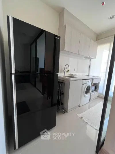 Modern kitchen with sleek black fridge, washing machine, and ample storage space.