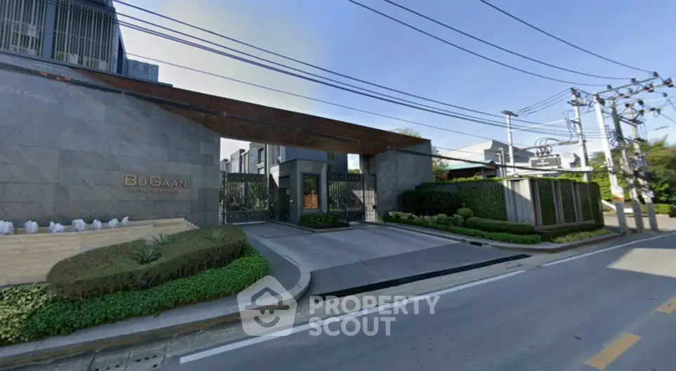 Modern gated entrance of luxury residential complex with lush landscaping and sleek architectural design.