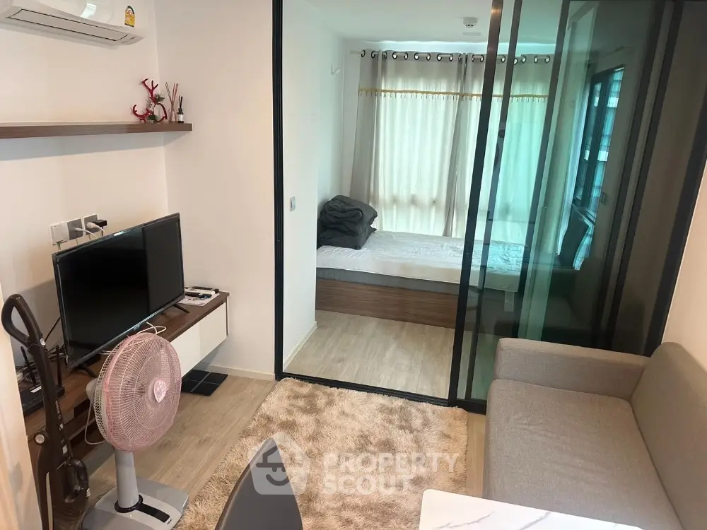 Modern compact living room with glass partition to bedroom, featuring cozy decor and natural light.