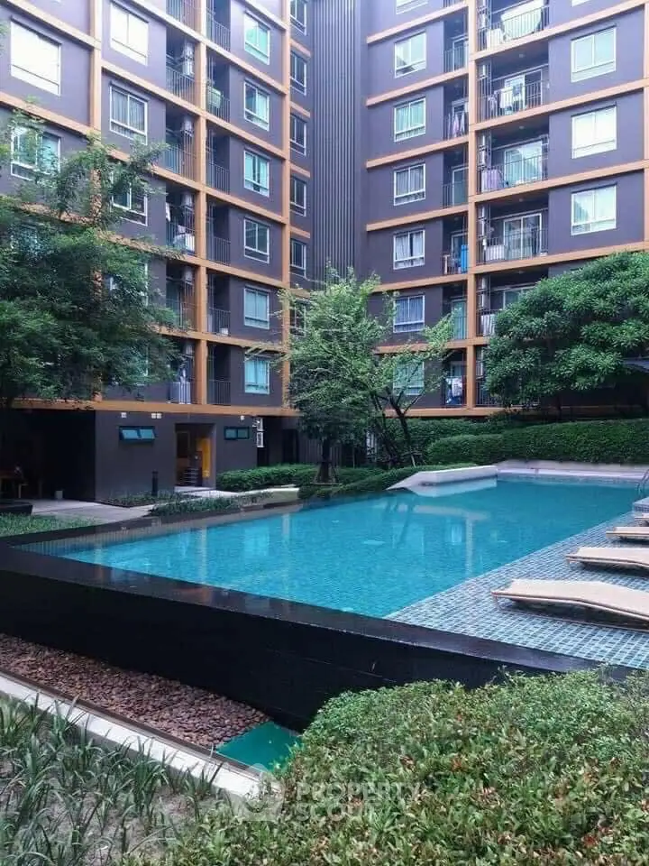 Luxurious residential complex with a serene pool area surrounded by lush greenery and modern apartment facades, offering a tranquil urban retreat.