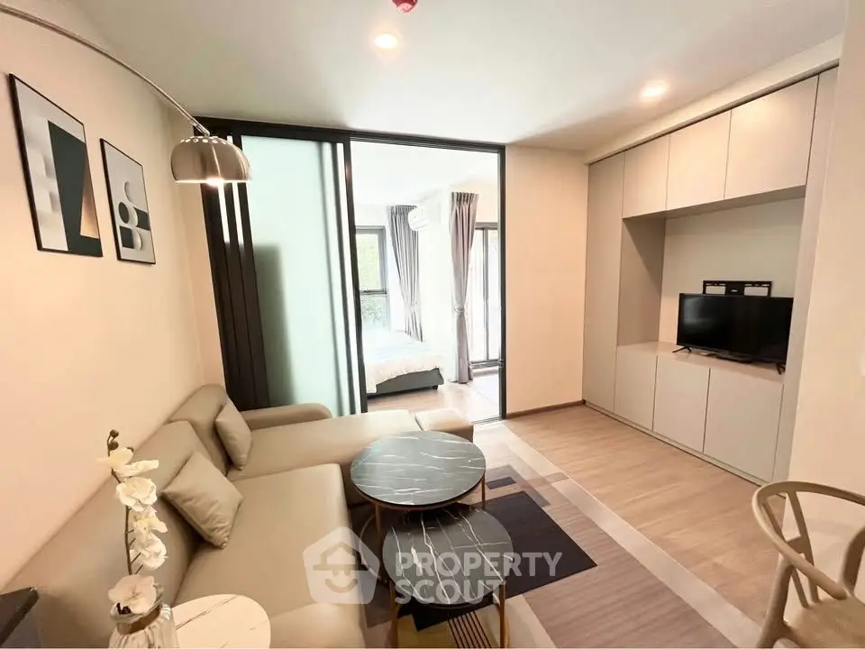 Modern living room with stylish decor and open view to bedroom, featuring sleek furniture and natural light.