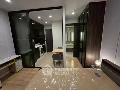 Modern bedroom with glass partition, stylish furniture, and view into kitchen and bathroom.