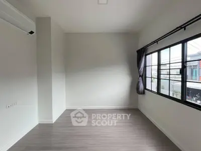 Spacious empty room with large window and modern flooring, perfect for customization.