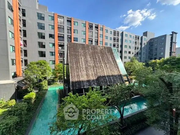 Modern apartment complex with lush garden and pool view under clear blue sky.