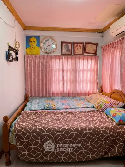 Cozy bedroom with wooden bed frame and pink curtains, featuring a wall clock and framed photos.