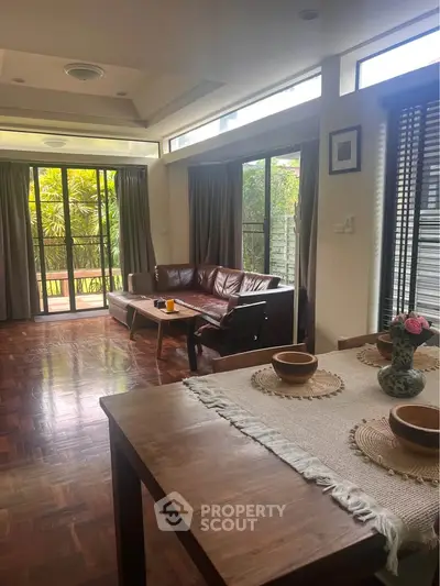 Spacious living room with large windows and garden view, featuring elegant wooden flooring and stylish furniture.