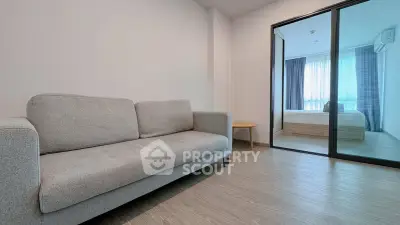 Modern living room with sleek sofa and glass partition leading to a bright bedroom.