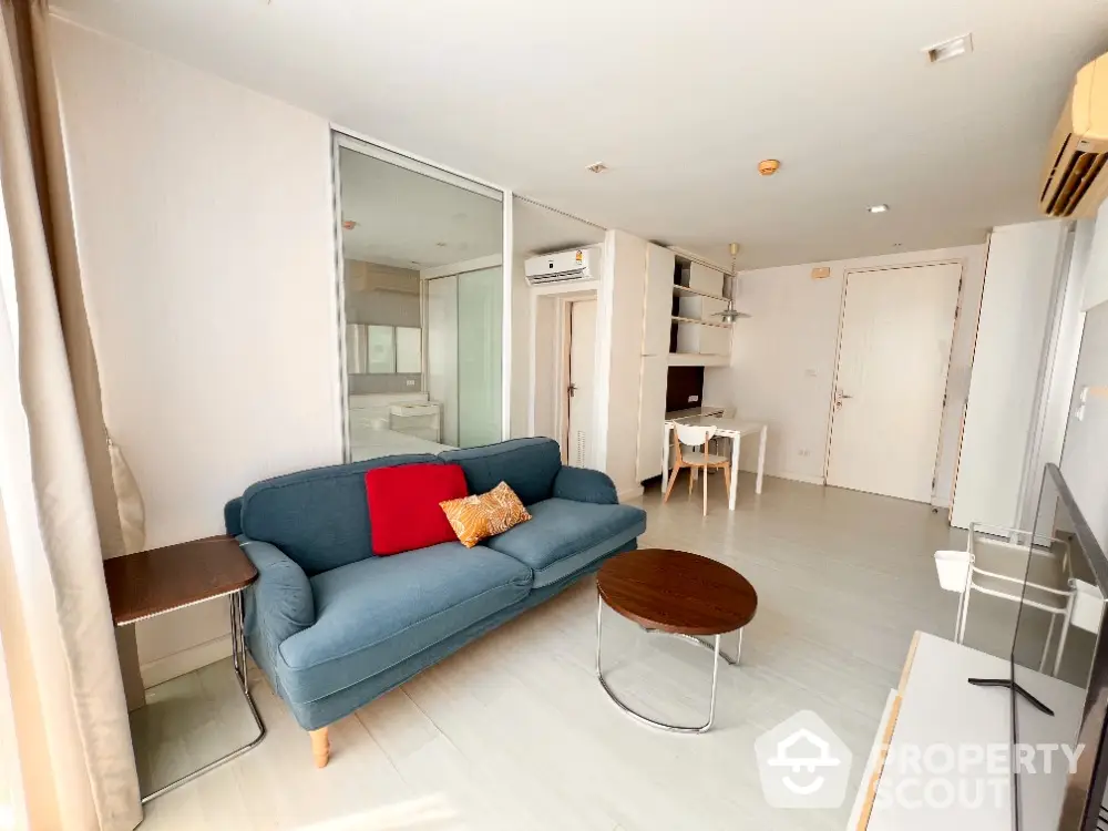 Spacious and modern open-plan living area with a sleek kitchen, comfortable blue sofa, and ample natural light, perfect for urban living.