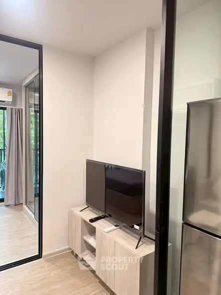 Modern apartment interior with sleek TV setup and glass sliding doors leading to a balcony.