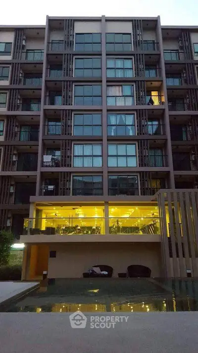 Modern apartment building with illuminated gym and pool area at dusk.