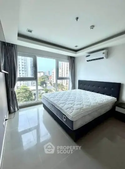 Spacious bedroom with large windows offering city views, featuring a modern bed and air conditioning.