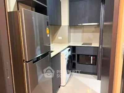 Modern kitchen with sleek appliances including fridge, washing machine, and microwave in compact layout.