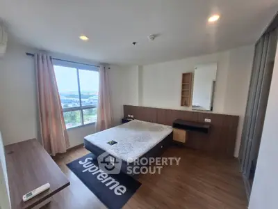 Spacious bedroom with large window and modern furnishings in high-rise apartment
