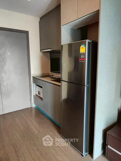 Modern kitchen with sleek fridge and built-in oven in compact apartment.