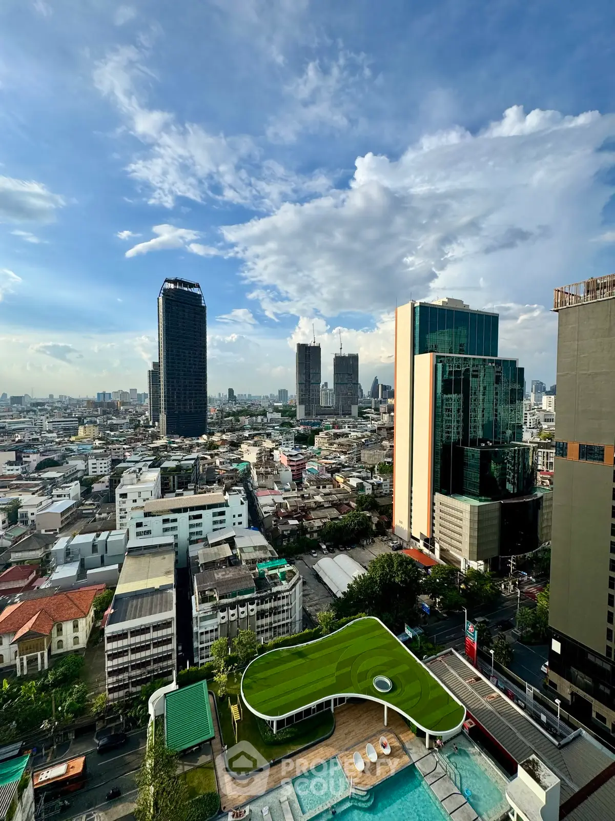 Stunning cityscape view from high-rise building with rooftop pool and lush green terrace.